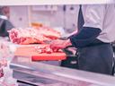Butcher trimming meat on a red cutting board behind a refrigerated display counter