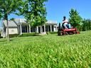 man mowing grass on riding lawnmower with house in background