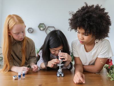 Three girls hovered over a microscope