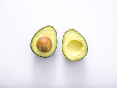 Two avocado halves on white background, one with pit and one with pit removed.
