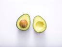 Two avocado halves on white background, one with pit and one with pit removed.