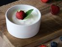 White ramekin of yogurt topped with a strawberry and mint on a wooden board with berries