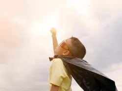 Boy in sunglasses and black cape reaching upward toward the sky