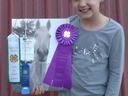 Girl holding horse photo with a purple ribbon and green ribbon reading "Best In Class."