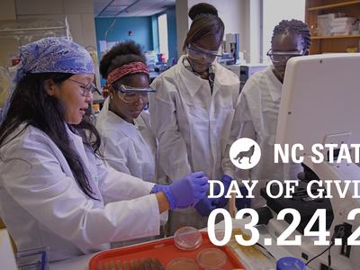 Five people in lab coats working at a microscope; overlaid text "NC STATE DAY OF GIVING 03.24.21"