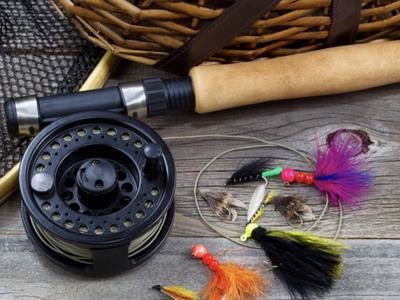 Fly fishing reel, rod handle, landing net, and colorful fishing flies on wooden surface