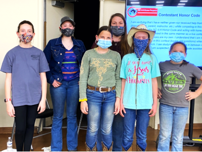 Seven masked children standing indoors in front of a screen titled "Contestant Honor Code."