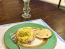 Eggs Benedict with hollandaise on a green-rimmed plate, vase of daffodils behind