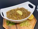 White bowl of cooked lentils with lemon wedge on wooden board, loose lentils and cilantro