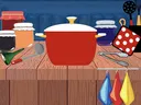 Red cooking pot with lid on wooden counter surrounded by jars, ladle, tongs, and potholder