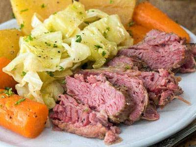 Sliced corned beef with cabbage, potatoes, and carrots served on a white plate