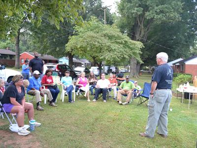 Man standing addressing a seated neighborhood group on a front lawn