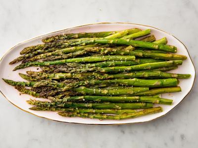 Roasted asparagus spears arranged on a white platter, sprinkled with coarse salt