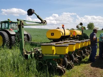 John Deere tractor towing MaxEmergePlus planter while workers load seed bags