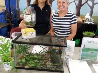 Two women at an NC State Extension booth with a terrarium and potted plants