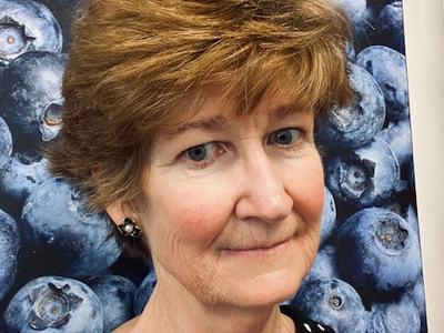 Woman with short brown hair in black polka-dot top against blueberry background