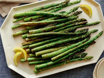 Grilled asparagus spears arranged on a white platter with two lemon wedges