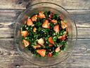 Glass bowl of kale salad with sliced strawberries, blueberries, and sunflower seeds