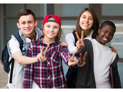 Four teenagers standing shoulder-to-shoulder outdoors making peace signs toward camera