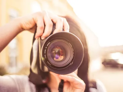 Person holding camera up, lens facing viewer (lens reads "Lens made in Japan")