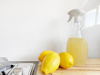 Spray bottle with yellow liquid and three lemons on a wooden cutting board