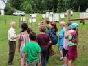 Man instructs a group of children near rows of beehives in a grassy field