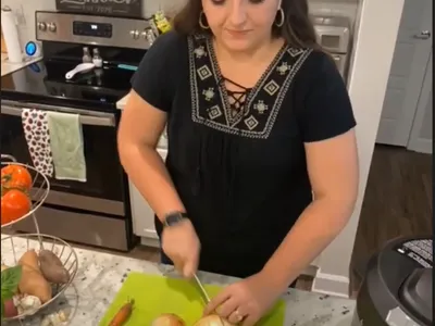 FCS agent holding knife and chopping onions. Vegetable stand in left of image with tomatoes, sweet potatoes, and other vegetables.