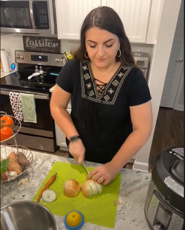 FCS agent holding knife and chopping onions. Vegetable stand in left of image with tomatoes, sweet potatoes, and other vegetables.
