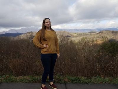 Woman standing on roadside overlook with rolling hills and cloudy sky in background