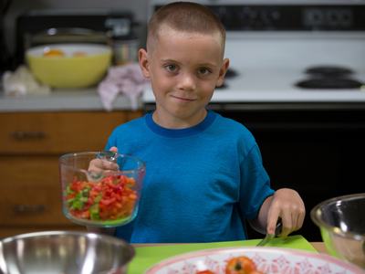 A boy prepares fruits and vegetables in the kitchen. A mystery fruit and veggie taste test is one activity families can try this summer as a way to spend quality time together.