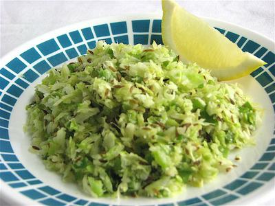 Shredded cabbage salad with cumin seeds and lemon wedge on blue-patterned plate