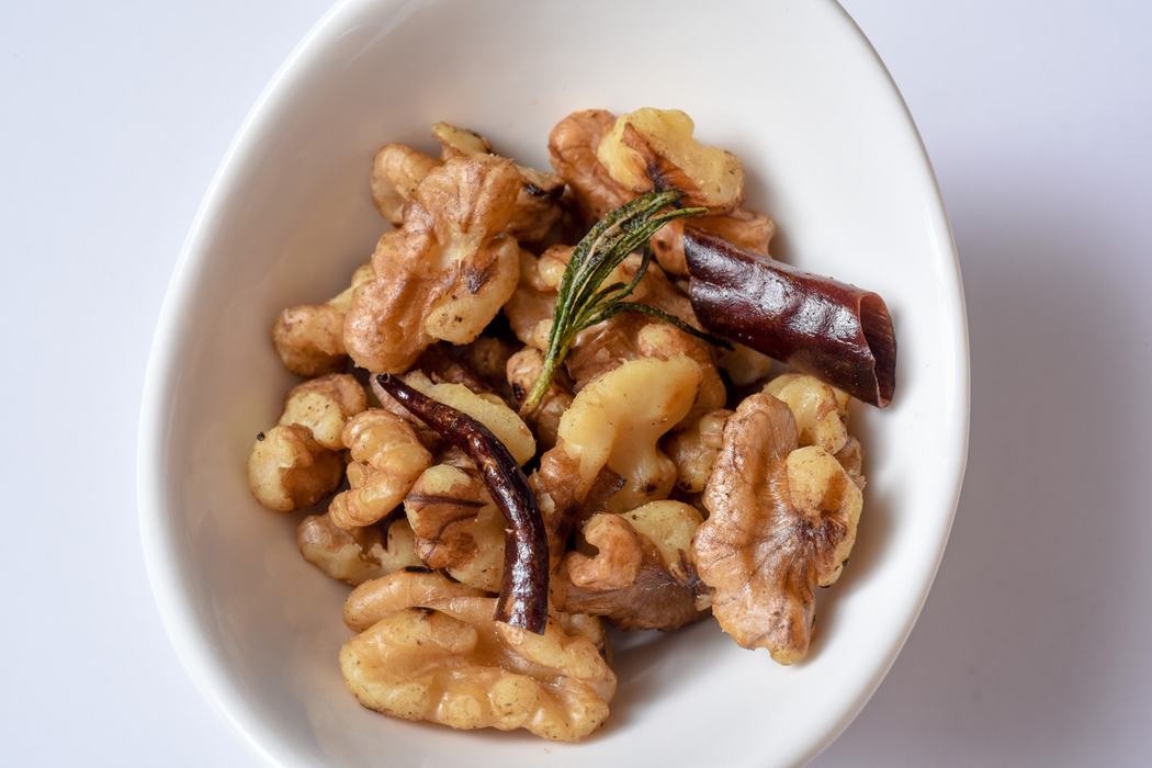 white bowl filled with walnuts, chili peppers, and a sprig of rosemary
