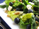 Green salad with blueberries, feta crumbles, and walnut pieces on a white plate
