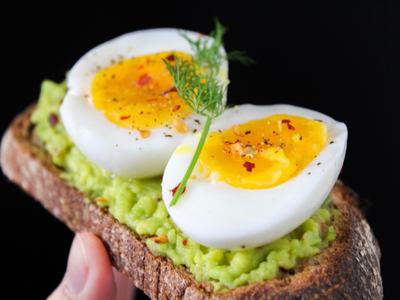 Slice of toast with mashed avocado topped by two halved soft-boiled eggs and a dill sprig