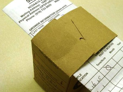 Soil sample submission form partially inserted into a brown cardboard mailer labeled "SOIL SAMPLE"