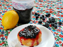 Doughnut topped with blueberry jam on a white plate, lemon and jar of jam nearby