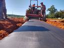 Tractor laying black plastic mulch over red soil while two workers guide it