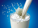 Milk being poured into clear glass with milk splashing out of glass into blue background.