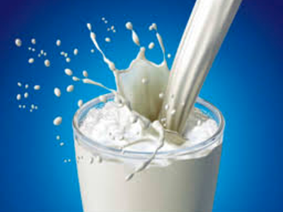Milk being poured into clear glass with milk splashing out of glass into blue background.