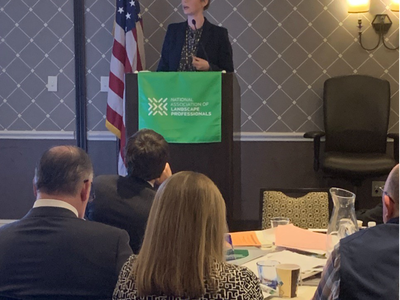 Speaker at podium with US flag and banner reading National Association of Landscape Professionals