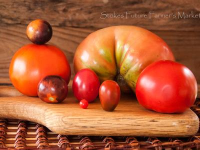 Assorted tomatoes arranged on wooden cutting board, text "Stokes Future Farmer's Market"