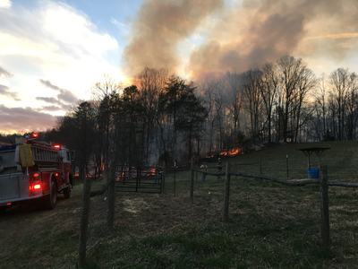 Wildfire burning along a treeline with heavy smoke, a fire truck and firefighters nearby