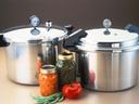 Two stainless steel pressure cookers with jars of canned vegetables and a tomato