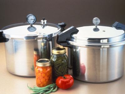 Two stainless steel pressure cookers with jars of canned vegetables and a tomato