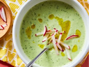 Bowl of green creamy soup topped with sliced radishes and drizzled olive oil, spoon inside