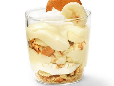Glass with layered banana pudding: vanilla custard, banana slices, whipped cream, and vanilla wafer