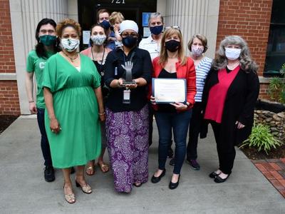 Group of masked adults standing outside, one holding a trophy and another a certificate