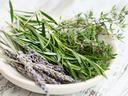 White bowl holding sprigs of rosemary, thyme with small pink flowers, and dried lavender
