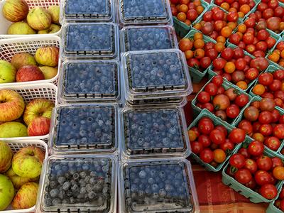 Apples in white baskets, blueberries in plastic clamshells, and cherry tomatoes in green cartons