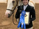 Equestrian in helmet holding blue ribbon and plaque reading "Champion" beside paint horse